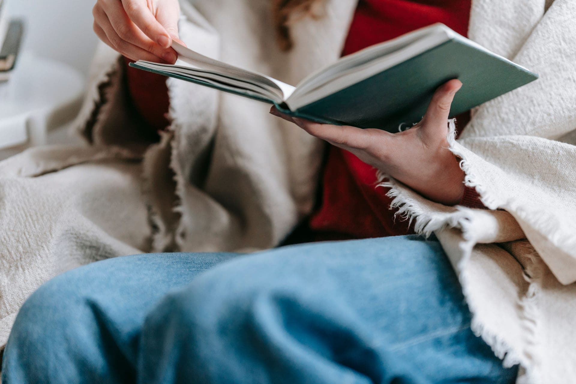 Someone reading in an armchair with a blanket over their knees