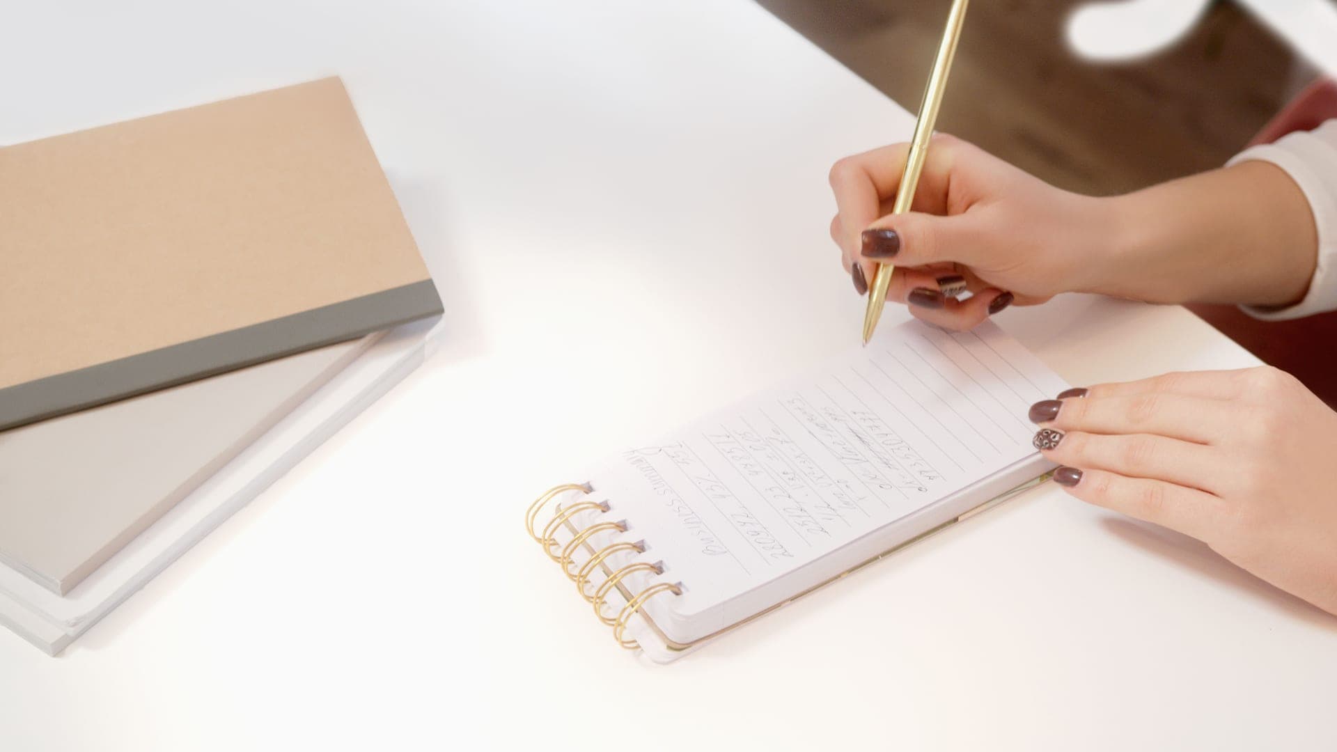 A hand writing in an open notebook on a wooden desk